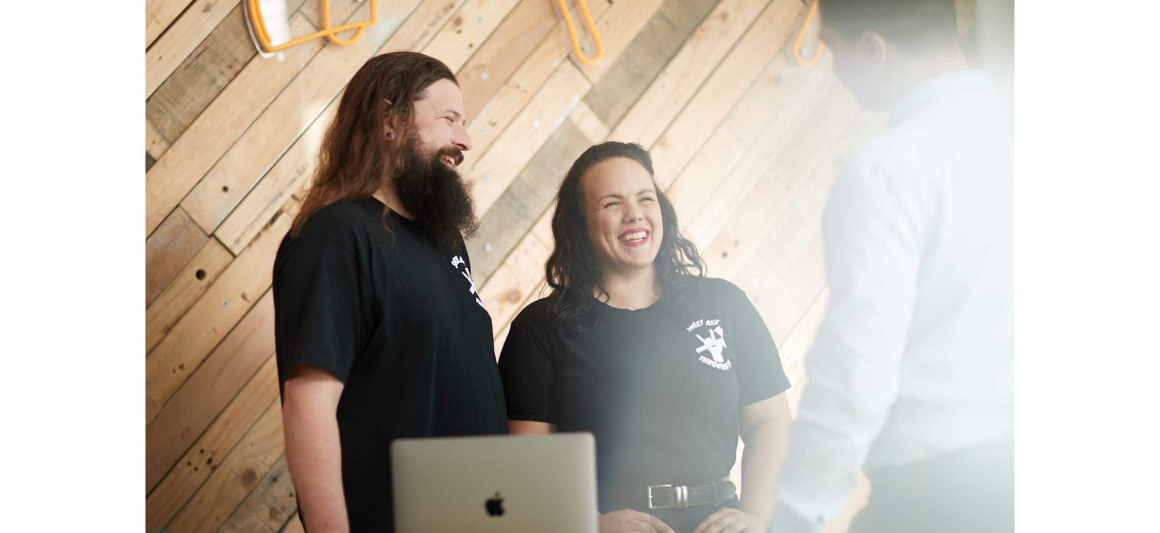 Sweet Axe Throwing owners Lloyd and Sarah smiling behind a counter as they talk to a customer.